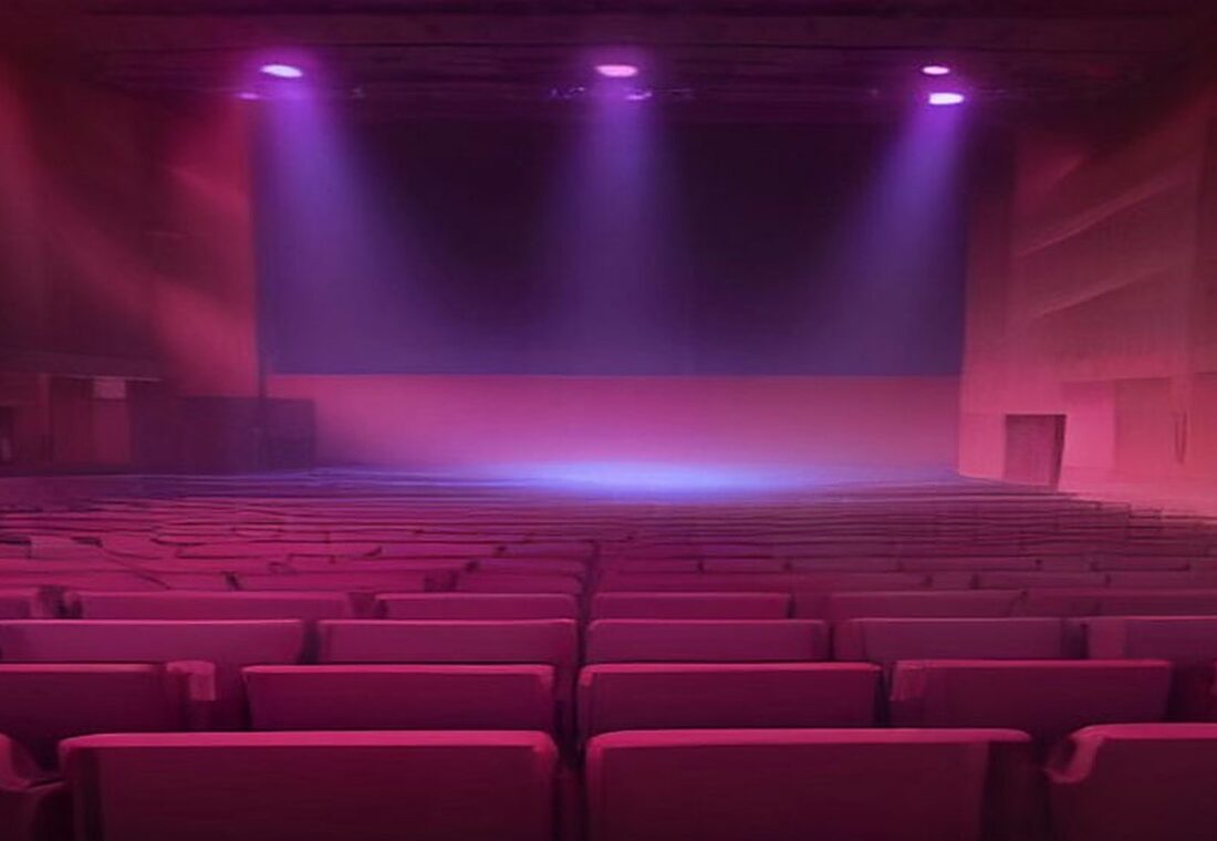 Auditorio de conciertos vacío con filas de butacas rojas y un escenario iluminado con luces rosas y moradas entre bruma