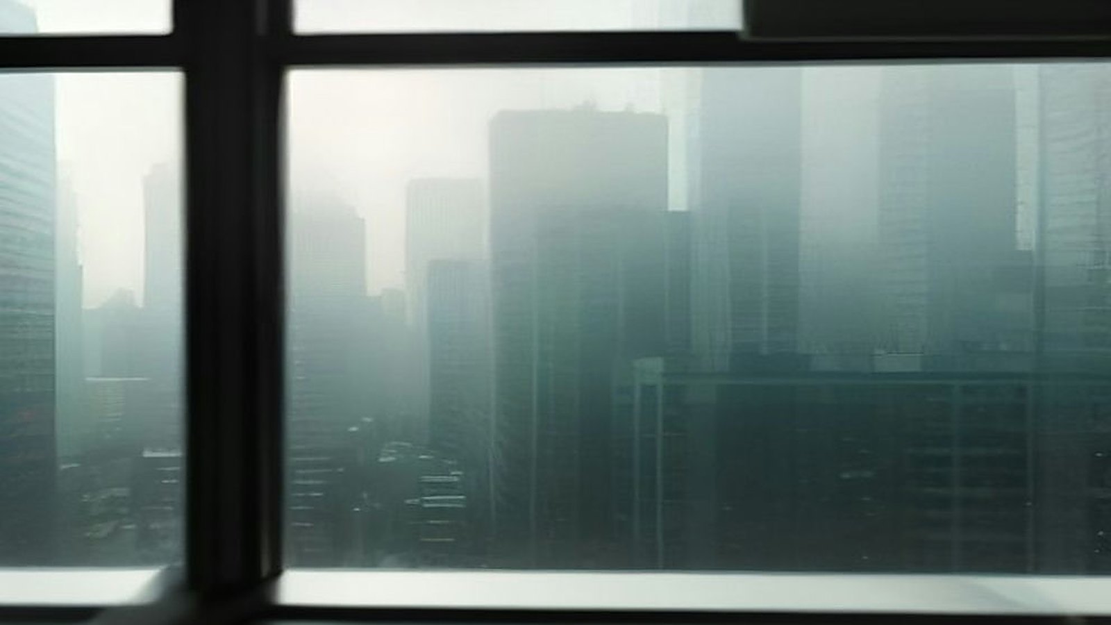 Vista desde una ventana alta hacia un horizonte de edificios envueltos en neblina grisácea, con el marco oscuro en primer plano