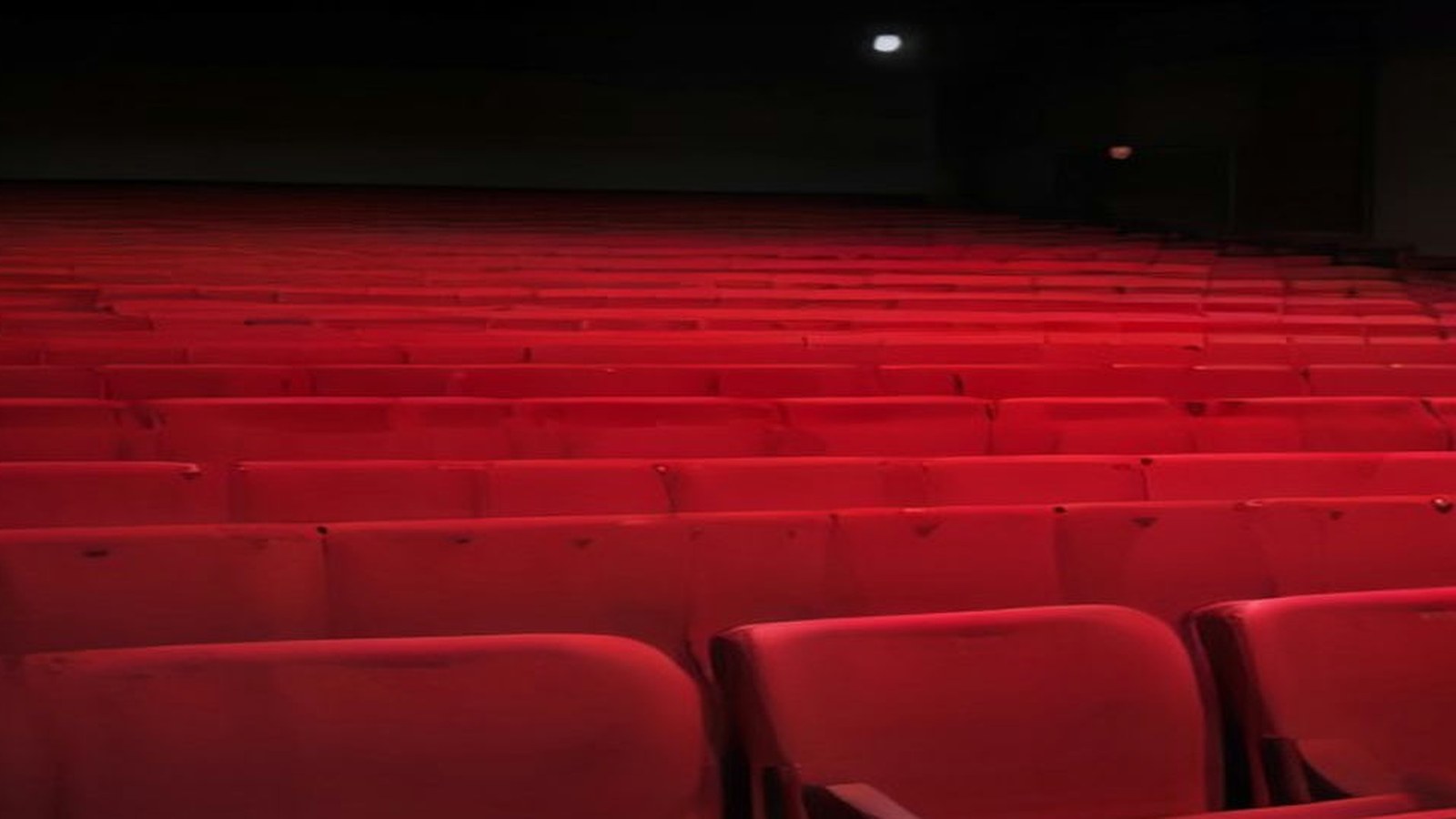 Auditorio vacío con filas de butacas rojas iluminado con luz cálida tenue