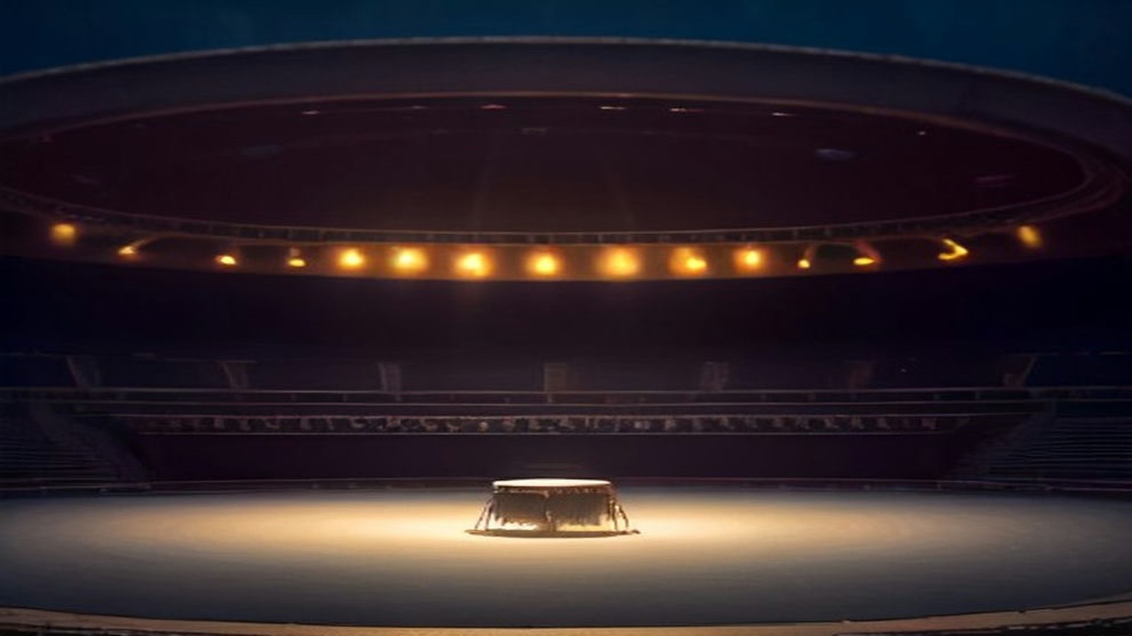 Ruedo vacío de una plaza de toros convertida en sala de conciertos, con un escenario circular al centro iluminado por luces cálidas al anochecer