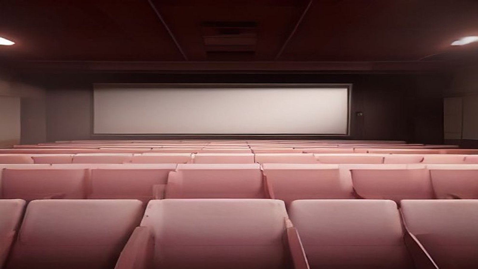 Sala de cine vacía con filas de butacas color rosa frente a una gran pantalla blanca encendida, en penumbra