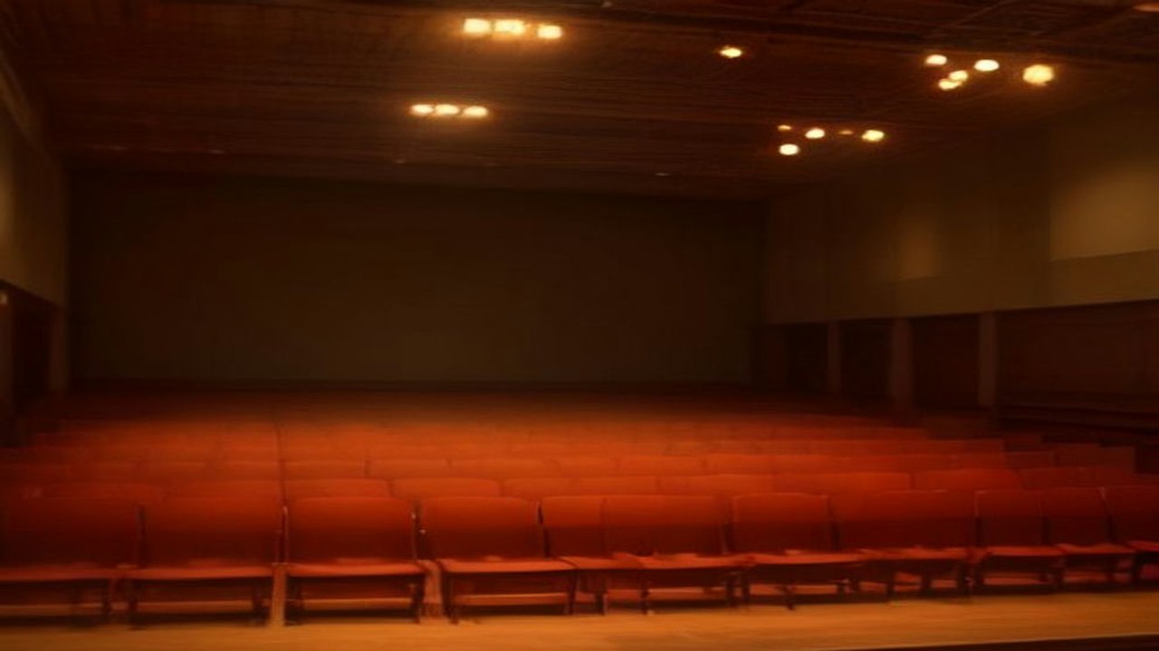 Auditorio vacío con filas de butacas rojas, muros de madera y luces cálidas en el techo