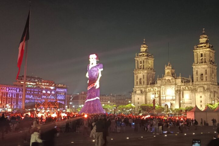 Catrina monumental iluminada en el Zócalo de la Ciudad de México, junto a la Catedral Metropolitana, de noche y con visitantes