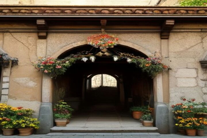 Fachada de una casona colonial con arco de piedra adornado con guirnaldas de flores y macetas de cempasúchil en la entrada