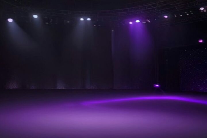 Escenario vacío de un club nocturno iluminado con reflectores morados que atraviesan la bruma