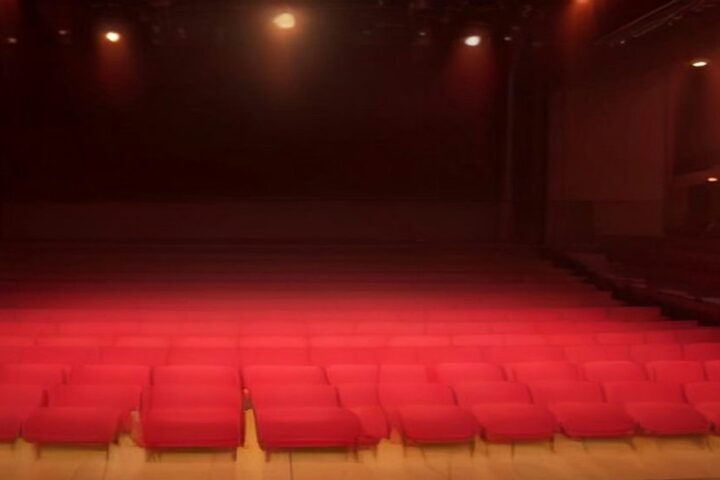 Escenario de una sala de conciertos preparado para mariachi y banda, con trompetas y violines en atriles, un sombrero de charro y luces cálidas