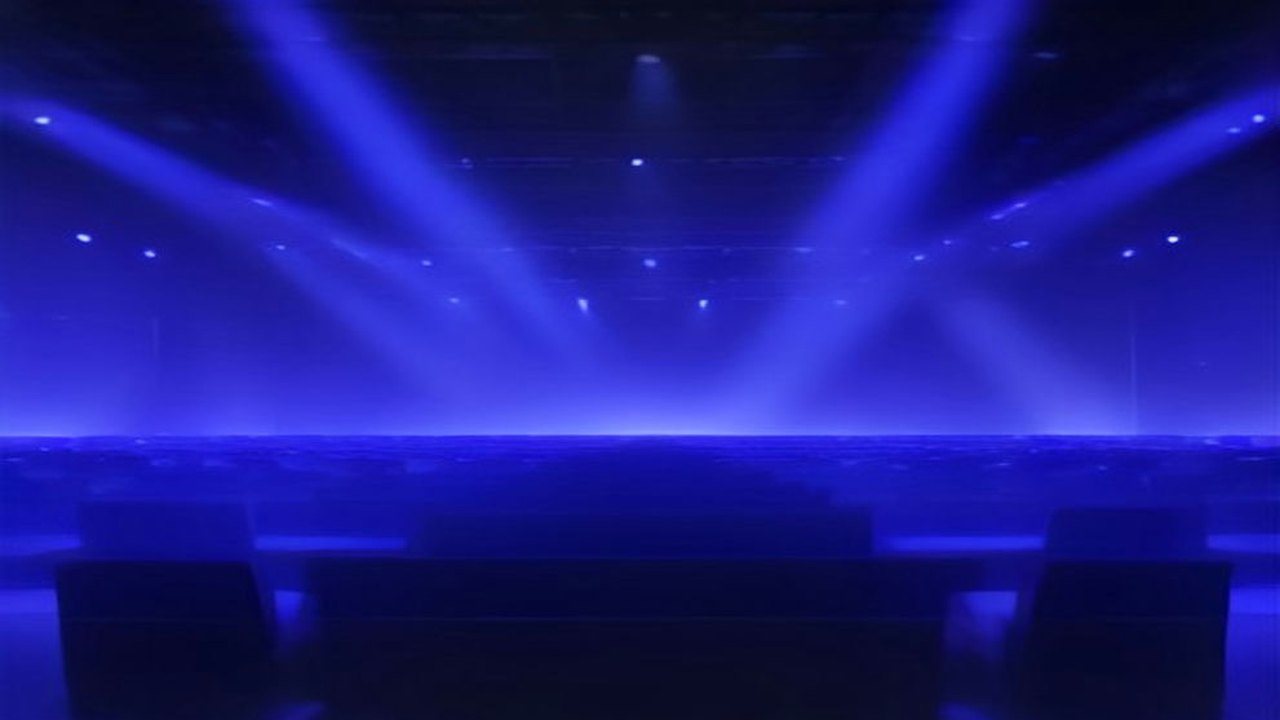 Arena de esports en penumbra con haces de luz azul y morada que atraviesan la bruma sobre un escenario y butacas vacías