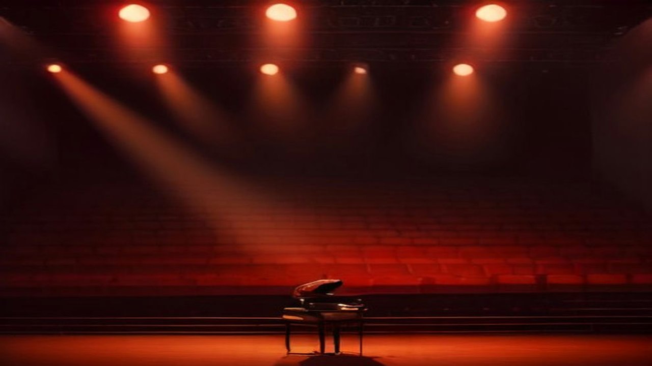 Escenario con un piano de cola iluminado por reflectores rojos y anaranjados frente a filas de butacas vacías