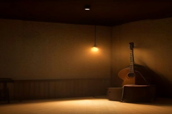 Escenario pequeño con una guitarra acústica recargada en un banco y una lámpara colgante de luz ámbar