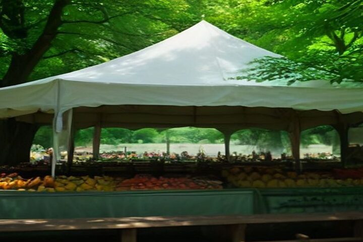 Mercado al aire libre bajo una gran carpa blanca en un jardín arbolado, con mesas largas llenas de frutas y verduras frescas de colores