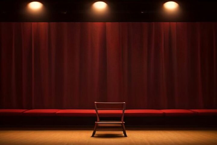 Escenario de comedia vacío con una silla de madera bajo reflectores cálidos y un telón de terciopelo rojo al fondo