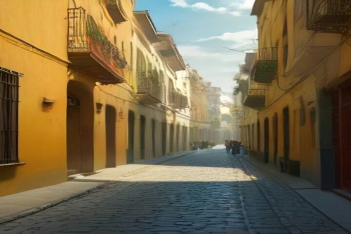 Calle empedrada de la Ciudad de México con edificios antiguos de fachadas amarillas, balcones de herrería y macetas, iluminada por el sol de la tarde