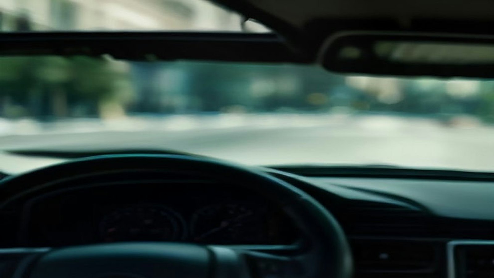 Volante y tablero de un automóvil estacionado con una calle de la ciudad desenfocada al fondo bajo luz de mañana