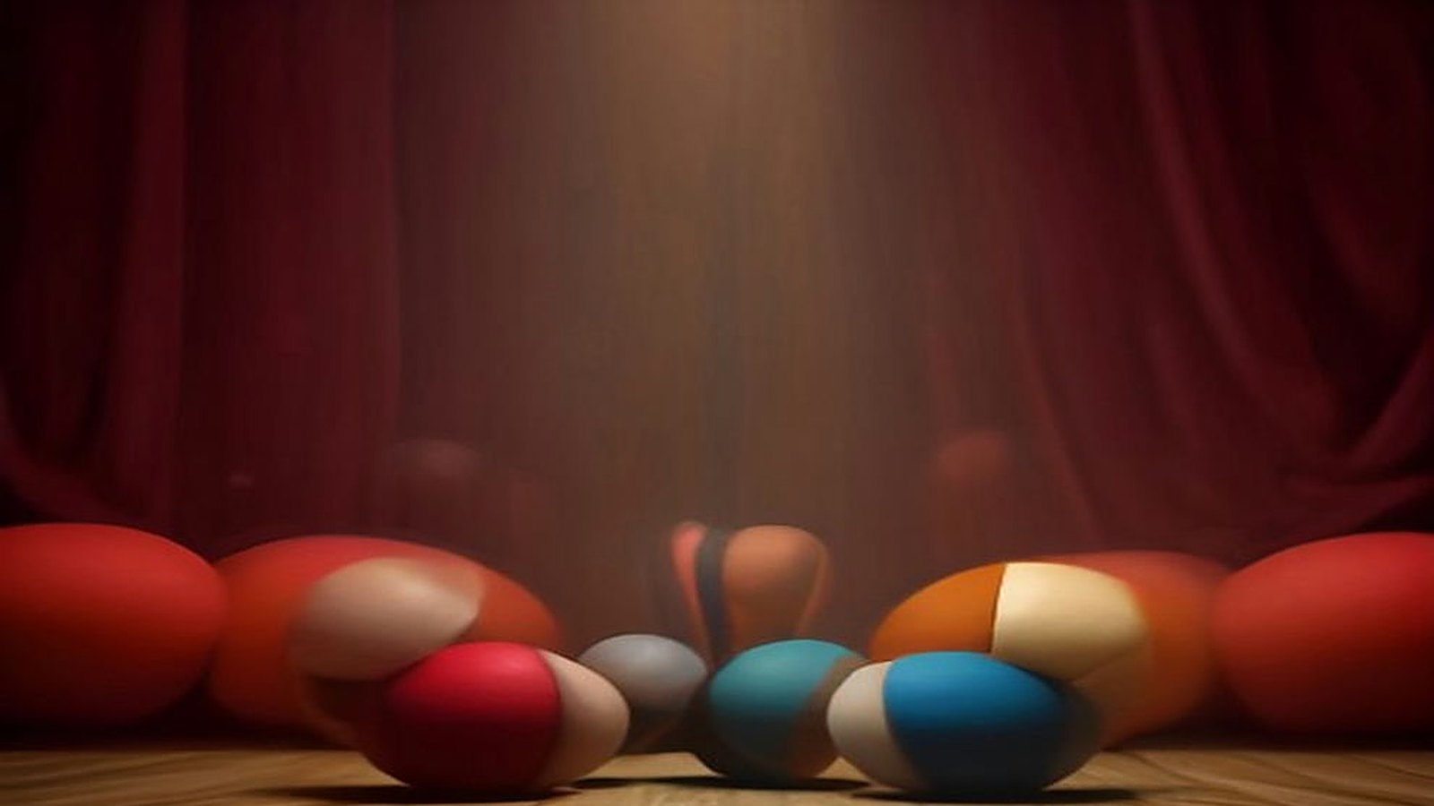 Pelotas de malabares de colores sobre el piso de madera de un escenario vacío, iluminadas por un reflector frente a un telón de terciopelo rojo