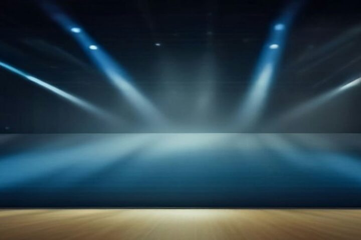 Recinto techado vacío preparado para un concierto con haces de luz azul que caen sobre el escenario entre humo