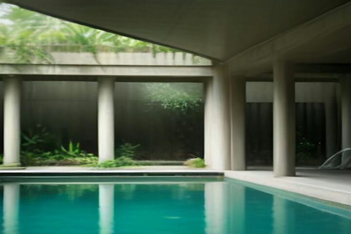 Patio de un museo de arquitectura moderna con una gran cubierta de concreto sostenida por columnas, plantas tropicales y un espejo de agua turquesa