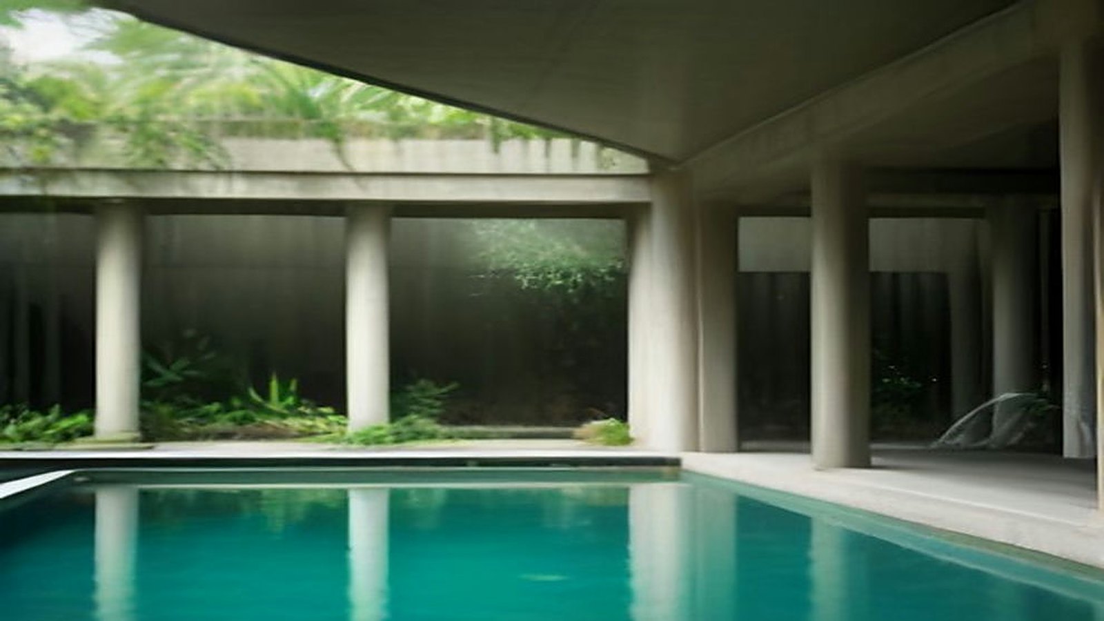 Patio de un museo de arquitectura moderna con una gran cubierta de concreto sostenida por columnas, plantas tropicales y un espejo de agua turquesa