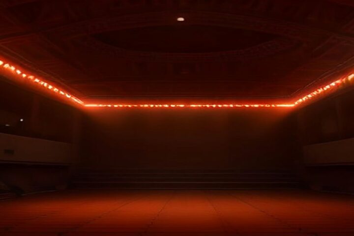 Recinto techado vacío con una línea de luces rojas y anaranjadas sobre la pista, listo para un concierto