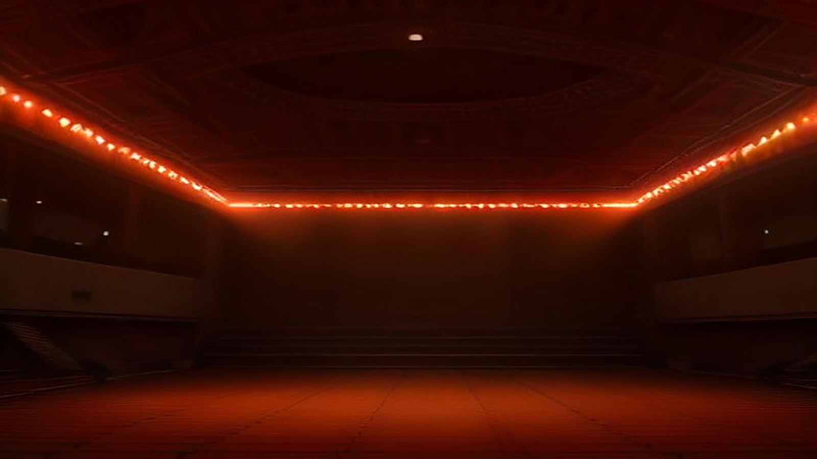 Recinto techado vacío con una línea de luces rojas y anaranjadas sobre la pista, listo para un concierto