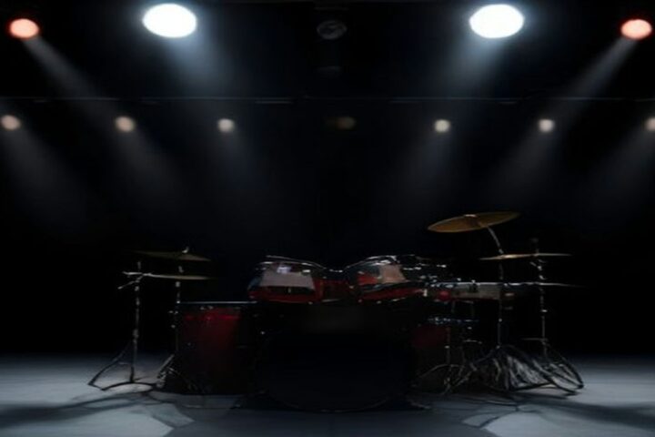 Escenario oscuro con una batería roja iluminada por reflectores blancos y rojos antes de un concierto de metal