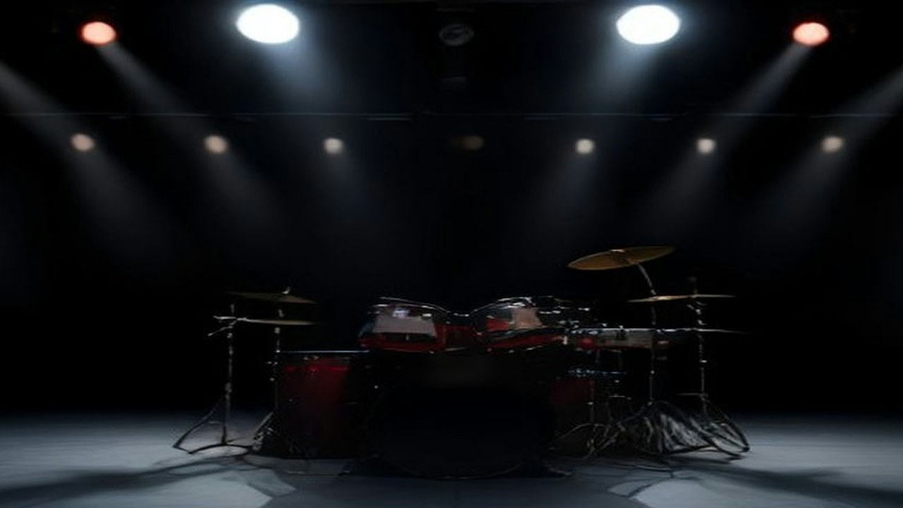 Escenario oscuro con una batería roja iluminada por reflectores blancos y rojos antes de un concierto de metal