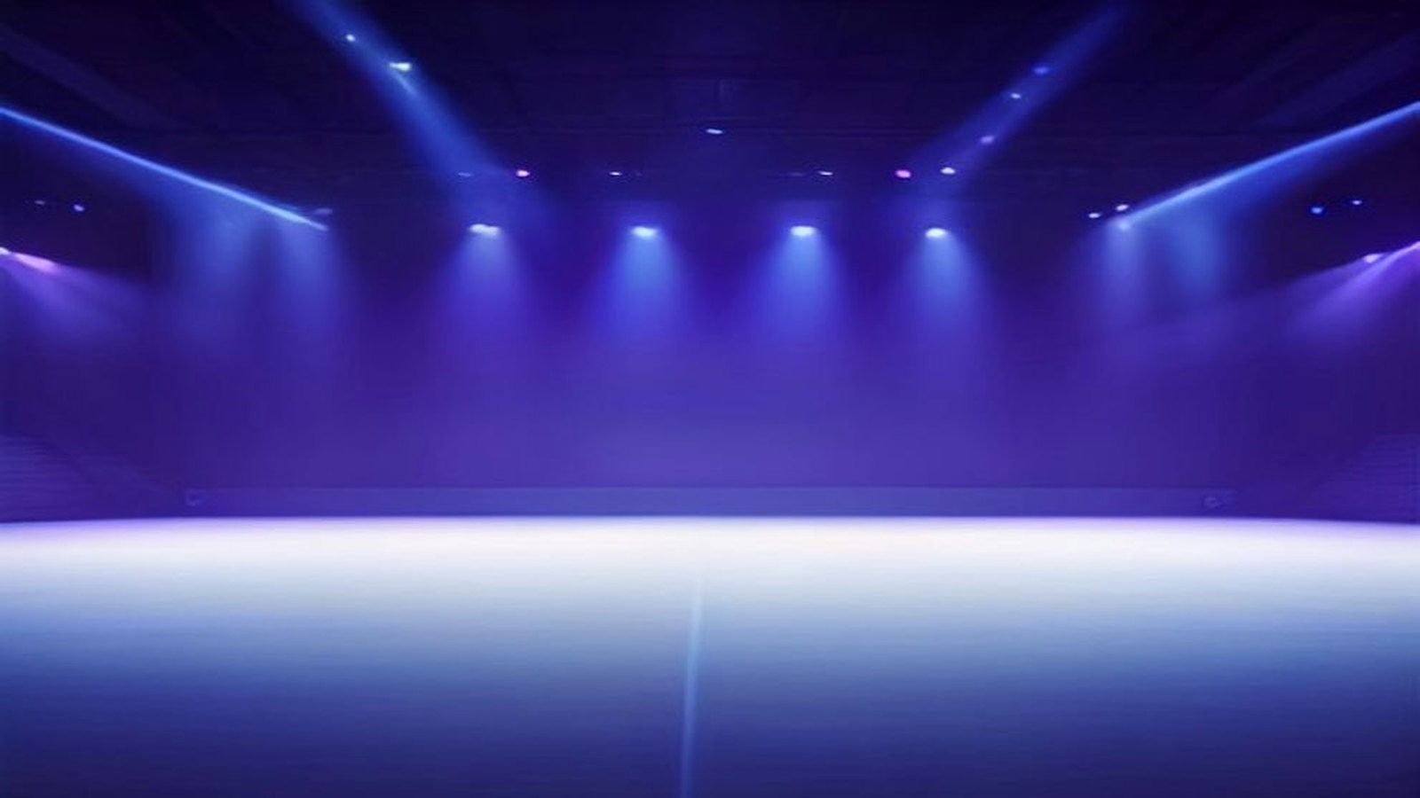 Escenario vacío de una arena de conciertos iluminado con reflectores azules y morados entre la bruma, sin público