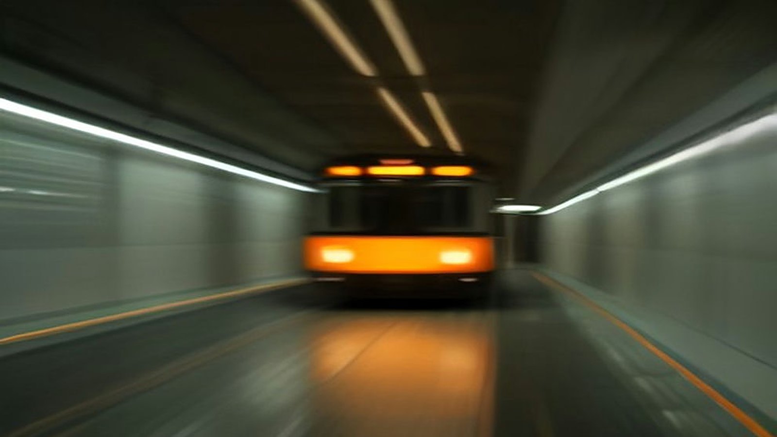 Tren naranja del Metro llegando a un andén subterráneo vacío, con luces del túnel en movimiento