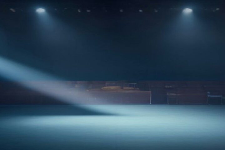 Escenario vacío de un recinto de conciertos con reflectores azules y haz de luz entre la bruma, sin público