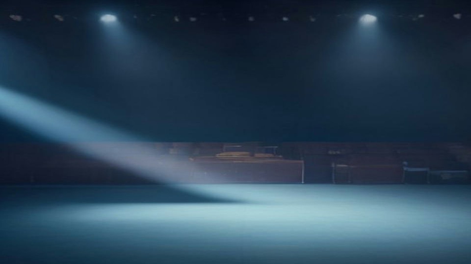 Escenario vacío de un recinto de conciertos con reflectores azules y haz de luz entre la bruma, sin público