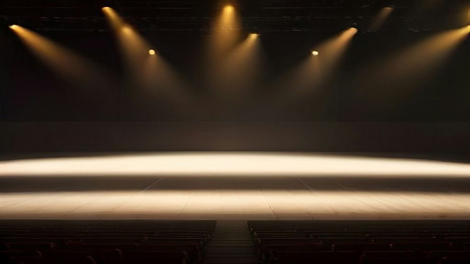 Escenario de concierto vacío con haces de luz ámbar que atraviesan la bruma y filas de butacas sin público en primer plano